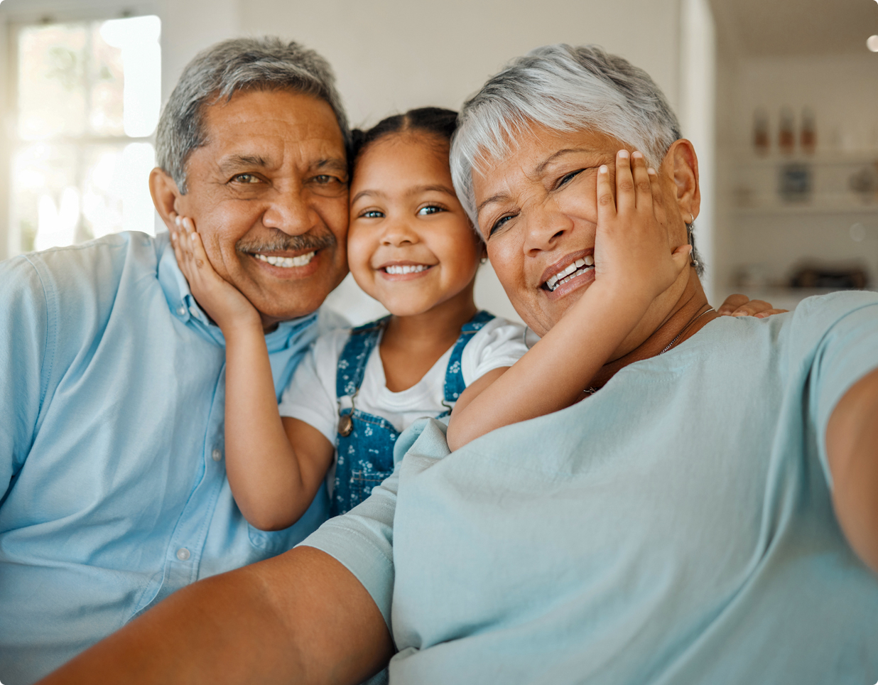 Grandchild holding a grandmother and grandfather's face, all smiling