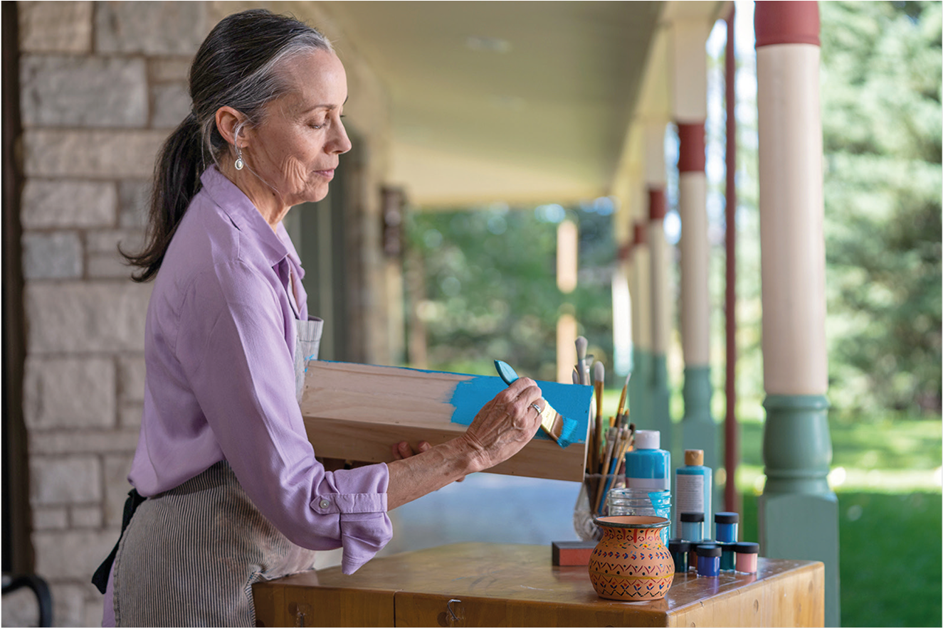 Older woman painting wood outside on a porch