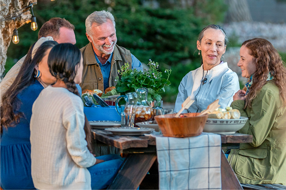 An older woman and man with family members sitting at a dining table outside