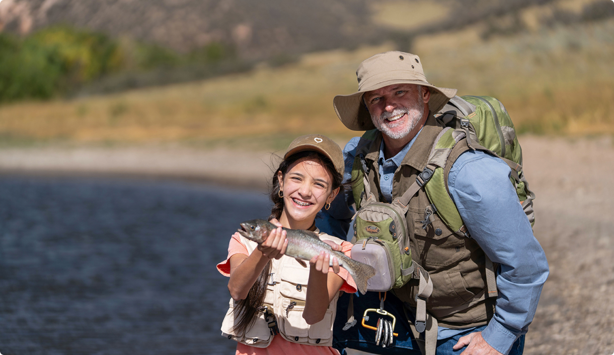 Grandfather with grandaughter holding a fish next to a lake